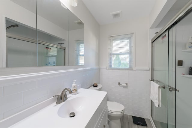 bathroom featuring a shower with door, vanity, tile walls, and toilet