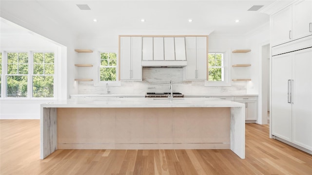 kitchen with a kitchen island with sink, white cabinets, a wealth of natural light, light hardwood / wood-style floors, and light stone counters