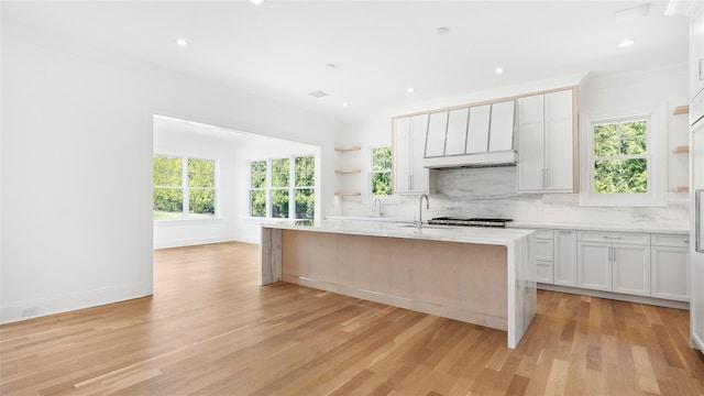 kitchen with a kitchen island with sink, plenty of natural light, white cabinets, and light hardwood / wood-style flooring