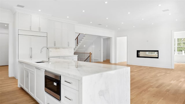 kitchen featuring light stone countertops, light hardwood / wood-style floors, white cabinetry, and stainless steel microwave