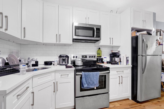 kitchen featuring appliances with stainless steel finishes, light hardwood / wood-style floors, white cabinetry, and tasteful backsplash