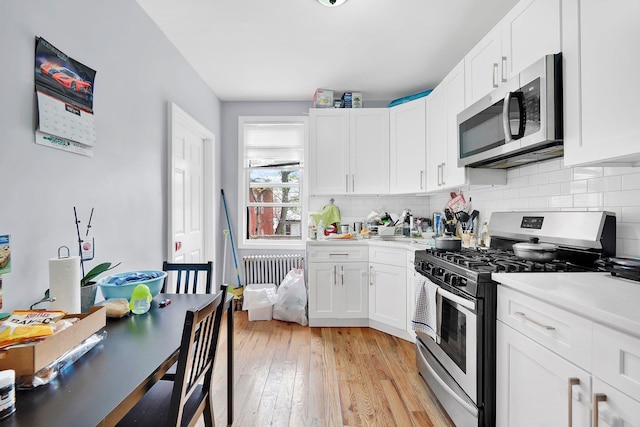 kitchen with white cabinetry, stainless steel appliances, radiator, and light hardwood / wood-style flooring