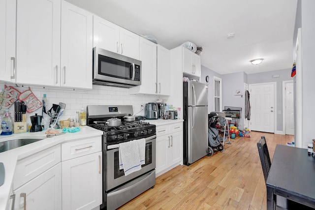 kitchen with decorative backsplash, white cabinetry, stainless steel appliances, and light hardwood / wood-style floors