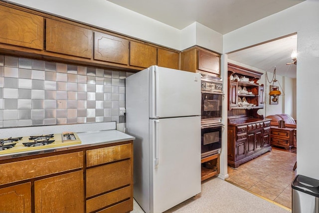 kitchen featuring light tile patterned flooring, white appliances, and backsplash