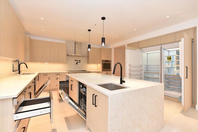 kitchen with stainless steel oven, a center island with sink, sink, light brown cabinetry, and decorative light fixtures