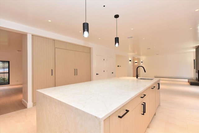 kitchen with light stone countertops, sink, pendant lighting, a kitchen island with sink, and light brown cabinetry