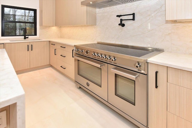 kitchen featuring tasteful backsplash, light brown cabinetry, range with two ovens, and sink