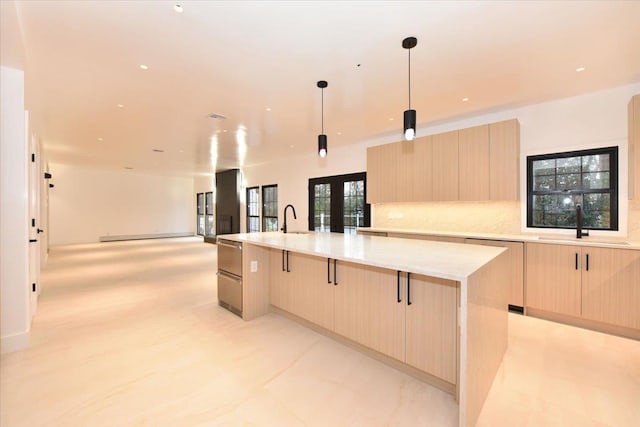 kitchen featuring decorative light fixtures, light brown cabinets, light stone counters, and a large island with sink