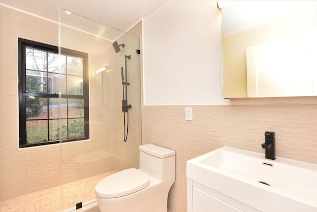 bathroom with tiled shower, vanity, tile walls, and toilet