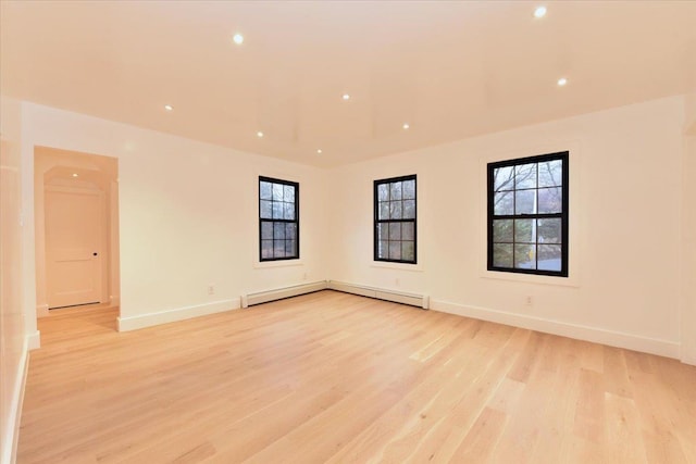 unfurnished room with baseboard heating, a healthy amount of sunlight, and light hardwood / wood-style floors