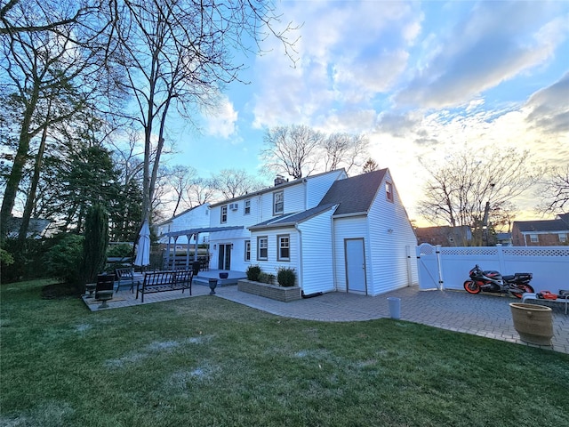 back house at dusk featuring a lawn and a patio