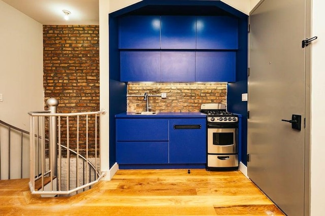 kitchen with dark countertops, blue cabinets, stainless steel gas range, light wood-style floors, and a sink