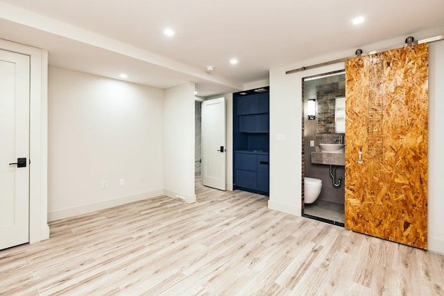 unfurnished bedroom featuring recessed lighting, ensuite bathroom, a barn door, wood finished floors, and baseboards