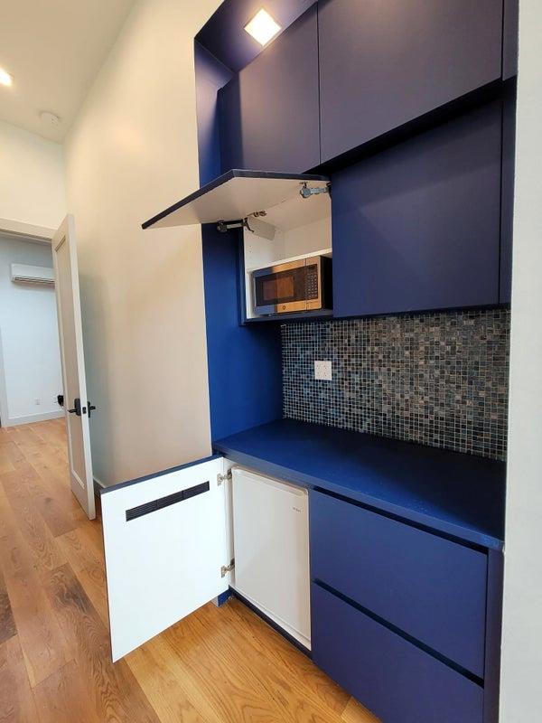 kitchen with tasteful backsplash, dark countertops, light wood-style flooring, stainless steel microwave, and an AC wall unit