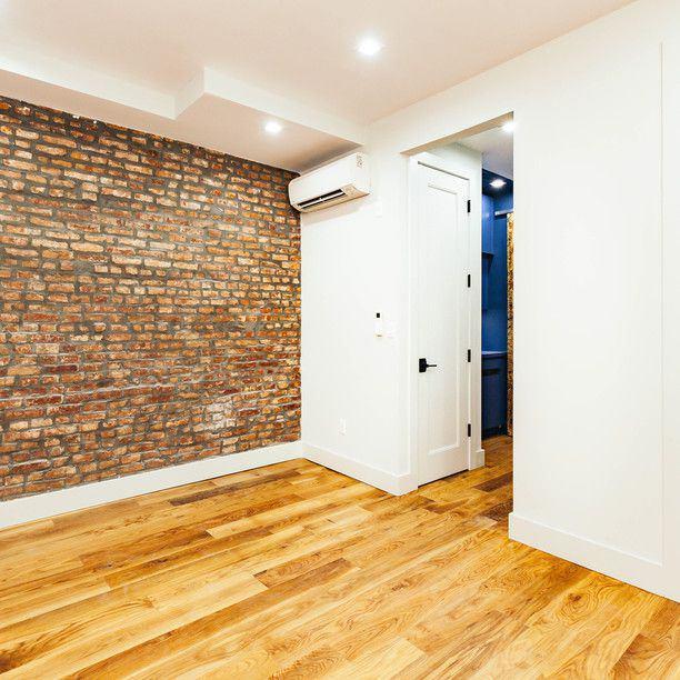 empty room featuring brick wall, light wood-style flooring, baseboards, and a wall mounted AC