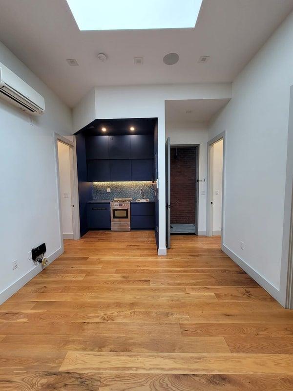 unfurnished living room featuring light wood-type flooring, a skylight, baseboards, and a wall mounted AC