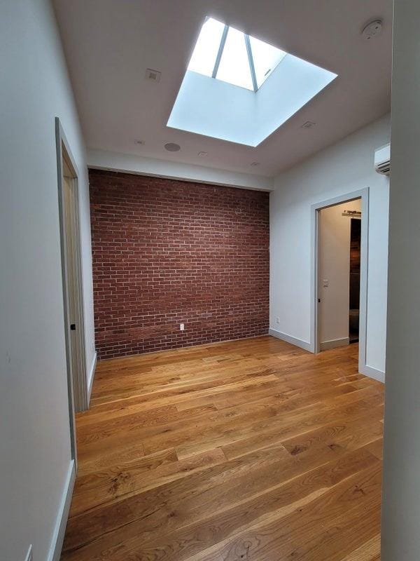 spare room featuring baseboards, light wood finished floors, brick wall, and a wall mounted AC