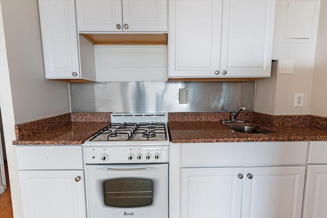 kitchen with dark stone countertops, white cabinetry, white gas stove, and sink