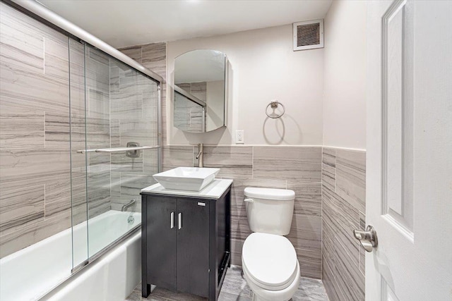 full bathroom featuring vanity, toilet, tile walls, and enclosed tub / shower combo