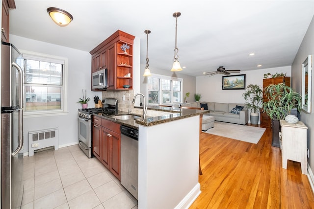 kitchen featuring appliances with stainless steel finishes, radiator, ceiling fan, decorative light fixtures, and light hardwood / wood-style floors