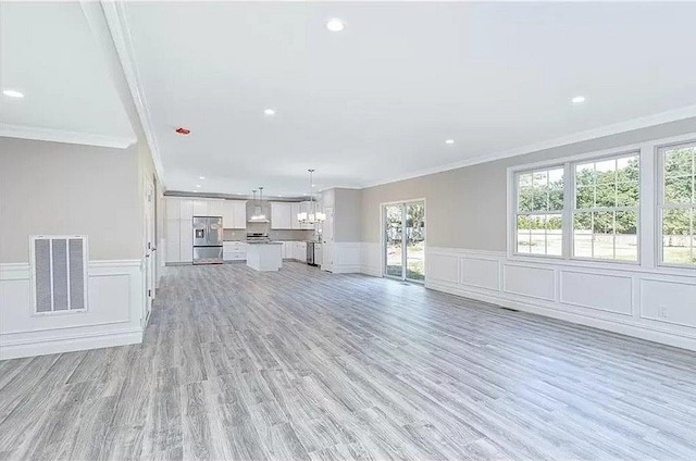 unfurnished living room with an inviting chandelier, ornamental molding, and light hardwood / wood-style flooring