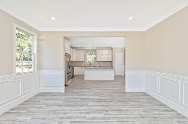 kitchen featuring light wood-type flooring, ornamental molding, a kitchen island, white cabinetry, and hanging light fixtures