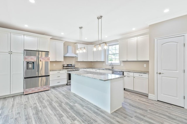 kitchen featuring appliances with stainless steel finishes, wall chimney range hood, decorative light fixtures, a center island, and white cabinetry