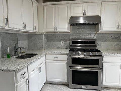 kitchen featuring range with two ovens, sink, tasteful backsplash, light stone counters, and white cabinetry