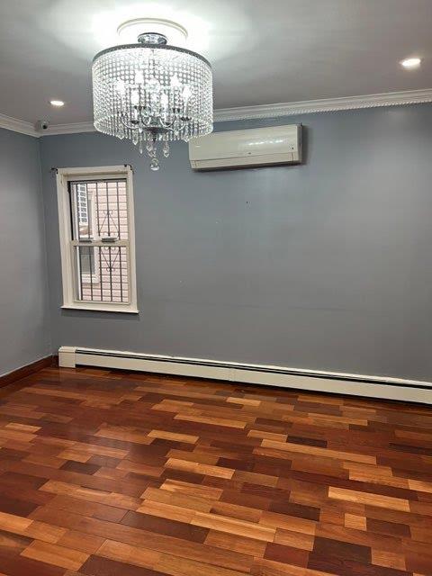 unfurnished dining area featuring ornamental molding, baseboard heating, a wall mounted AC, an inviting chandelier, and hardwood / wood-style floors