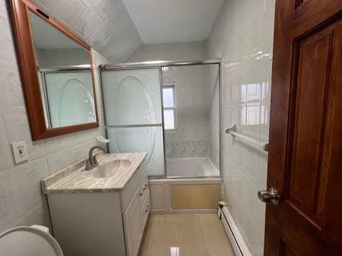 full bathroom featuring tile walls, a baseboard radiator, bath / shower combo with glass door, and lofted ceiling