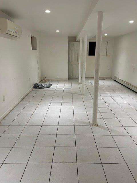 basement featuring an AC wall unit, light tile patterned floors, and a baseboard radiator