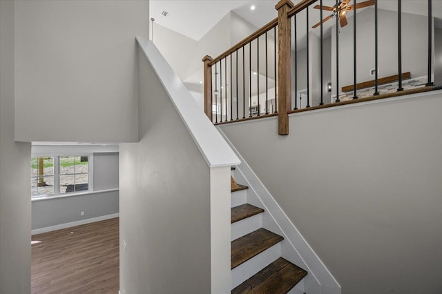 stairs with hardwood / wood-style floors, a towering ceiling, and ceiling fan