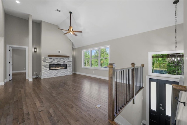 unfurnished living room featuring dark hardwood / wood-style floors, a stone fireplace, ceiling fan with notable chandelier, and high vaulted ceiling