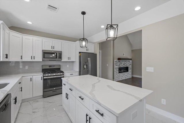 kitchen featuring appliances with stainless steel finishes, tasteful backsplash, decorative light fixtures, white cabinets, and a center island