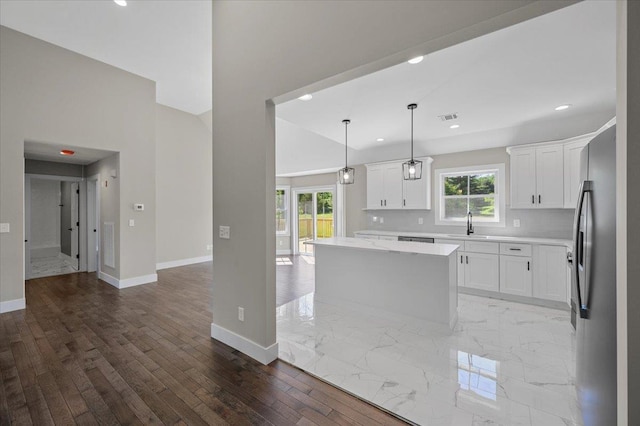 kitchen featuring white cabinets, stainless steel fridge, tasteful backsplash, decorative light fixtures, and a kitchen island