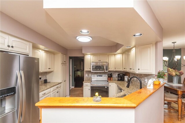 kitchen featuring backsplash, sink, appliances with stainless steel finishes, decorative light fixtures, and kitchen peninsula