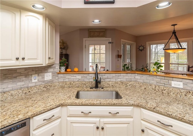 kitchen with backsplash, white cabinets, sink, stainless steel dishwasher, and decorative light fixtures