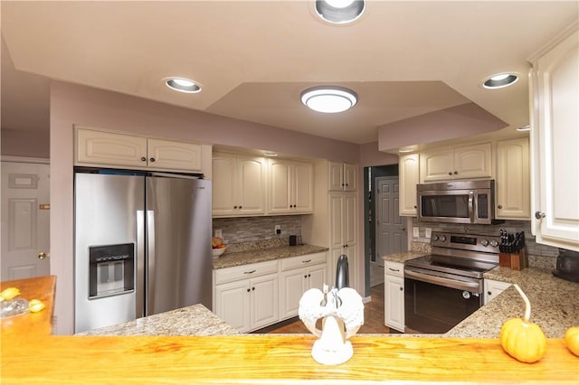 kitchen with kitchen peninsula, decorative backsplash, light stone countertops, and appliances with stainless steel finishes