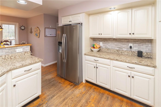 kitchen with dark wood-type flooring, decorative backsplash, stainless steel fridge, light stone countertops, and white cabinetry