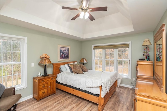 bedroom with ceiling fan, light hardwood / wood-style floors, and a raised ceiling