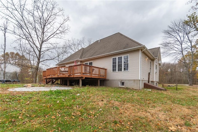 rear view of house with a wooden deck, a yard, and a trampoline