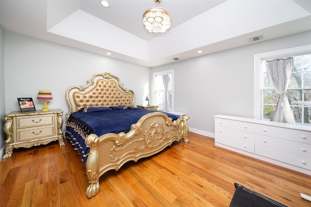 bedroom featuring a raised ceiling, multiple windows, and hardwood / wood-style floors