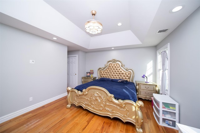 bedroom with wood-type flooring, a raised ceiling, and a closet