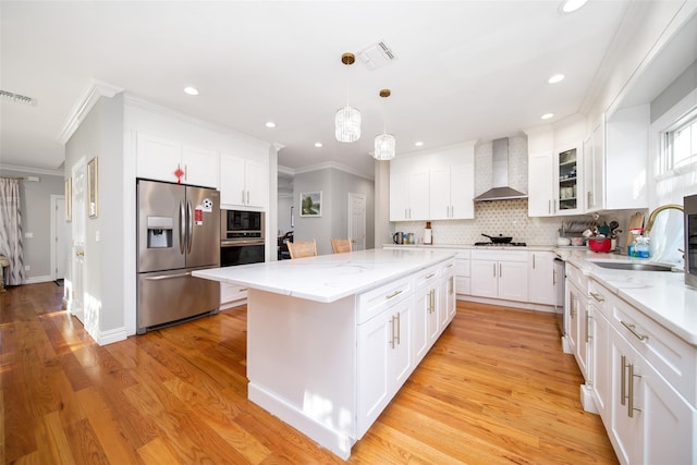 kitchen with white cabinetry, sink, wall chimney exhaust hood, a kitchen island, and appliances with stainless steel finishes