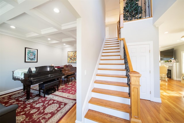 stairs featuring hardwood / wood-style floors, crown molding, coffered ceiling, and beam ceiling