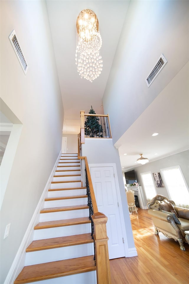 stairway with hardwood / wood-style flooring, a towering ceiling, and an inviting chandelier