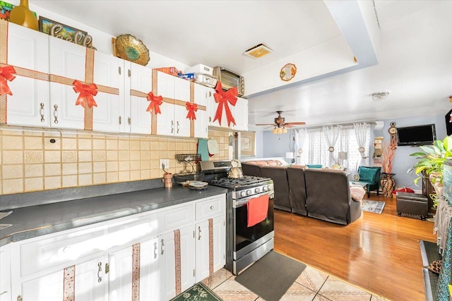 kitchen with white cabinets, ceiling fan, decorative backsplash, light hardwood / wood-style floors, and stainless steel range with gas stovetop