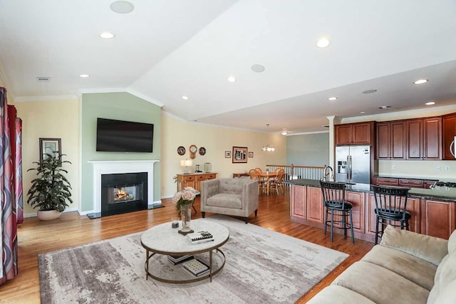 living room featuring vaulted ceiling, light hardwood / wood-style flooring, ornamental molding, and sink