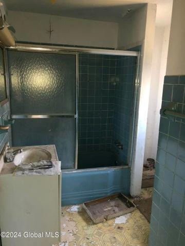 bathroom featuring vanity, tile walls, and bath / shower combo with glass door