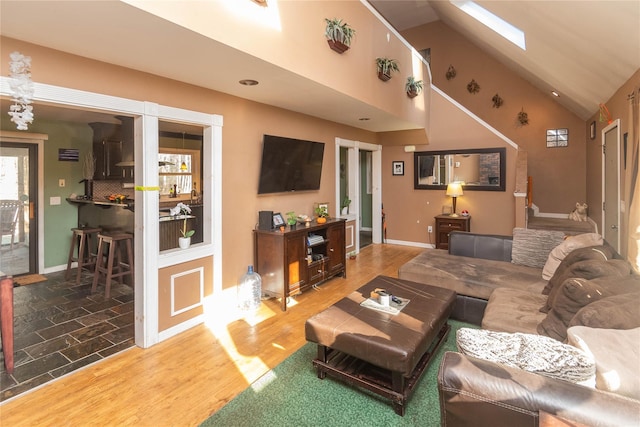 living room featuring hardwood / wood-style flooring, high vaulted ceiling, and a skylight